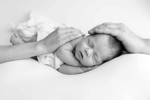 Nyf&oslash;dtfotografering - Baby sover p&aring; siden p&aring; et teppe og mamma og pappa holder hendene sine p&aring; baby