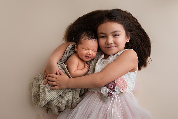 Stores&oslash;ster ligger p&aring; bakgrunn i fotostudio og holder rundt nyf&oslash;dt baby som ligger i armene hennes