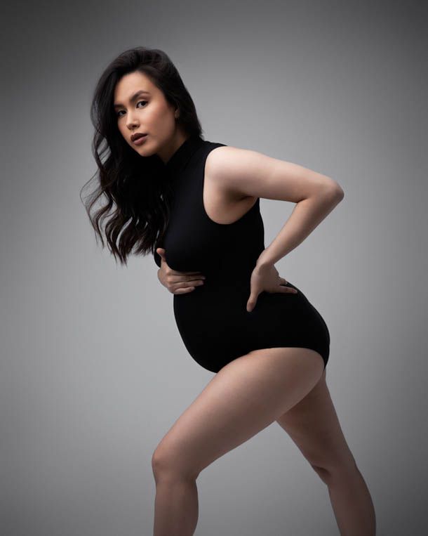 Dame med gravidmage og sort body poserer forran hvit bakgrunn i studio