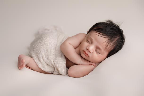 Nyf&oslash;dt jente sover p&aring; siden med hendene under hodet p&aring; et beige teppe med teppe rundt seg