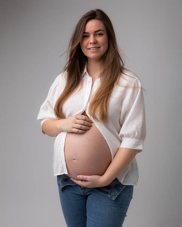 Snart mamma holder p&aring; gravidmagen forran hvit bakgrunn i fotostudio