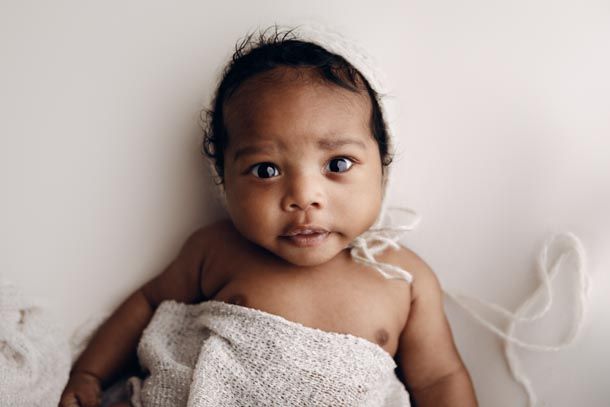 Nyf&oslash;dtfotografering - V&aring;ken baby med lue og skjerv over magen titter inn i kamera