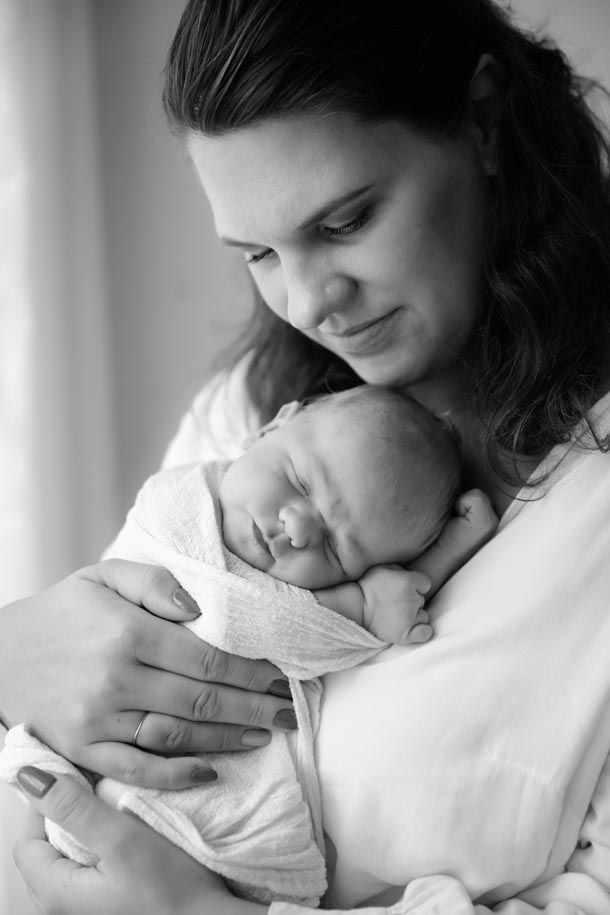 Nyf&oslash;dtfotografering - Mamma har nyf&oslash;dt baby inntil brystet ved vindu i studio