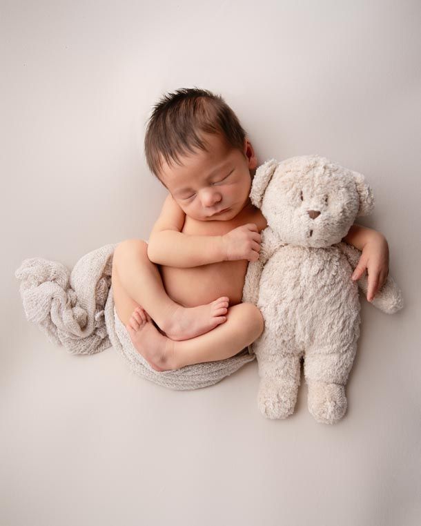 Nyf&oslash;dtfotografering - Sovende baby ligger p&aring; naturfarget teppe og holder rundt en bamse