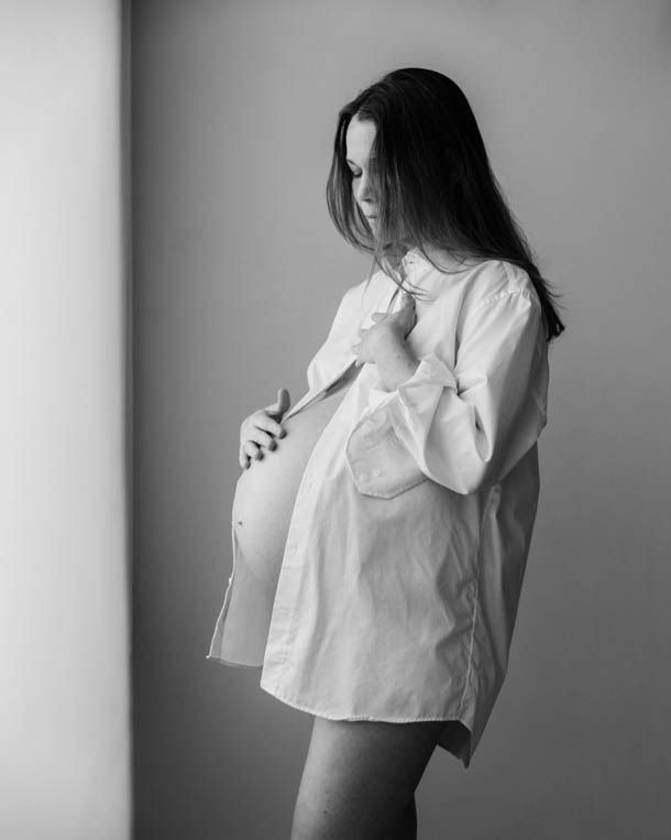 Dame med hvit skjorte holder p&aring; gravidmagen