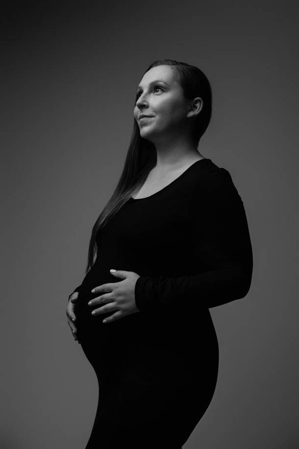 Gravid - Dame i sort kjole holder p&aring; magen og titter opp 