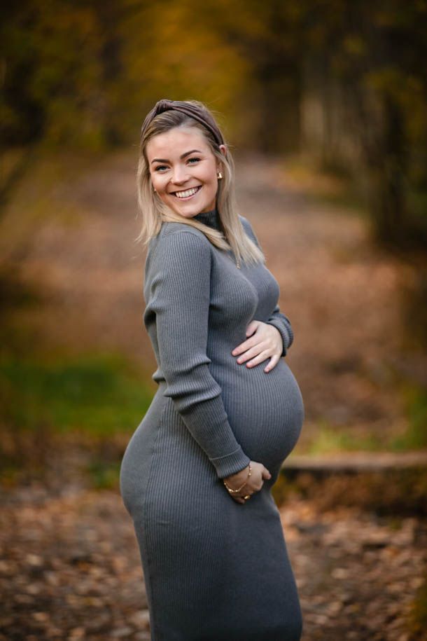 Gravidfotografering utend&oslash;rs - dame i gr&aring; kjole poserer p&aring; sti i skogen med h&oslash;stfarger og h&oslash;stblader