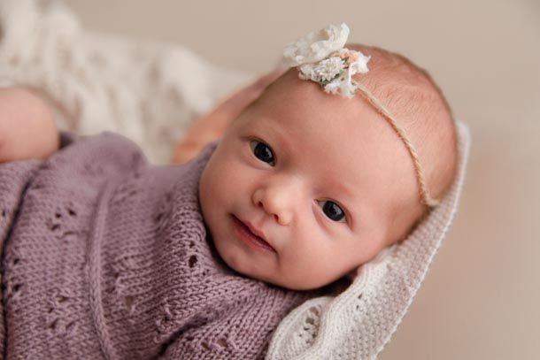 Nyf&oslash;dtfotografering -  V&aring;ken nyf&oslash;dt jente ligger p&aring; strikket teppe med h&aring;rb&aring;nd og ser inn i kamera