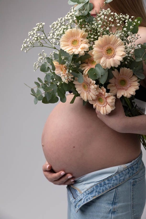 Gravidfotografering - Dame holder rundt gravidmagen med en h&aring;nd og holder blomsterbukett i den andre h&aring;nden foran magen. 