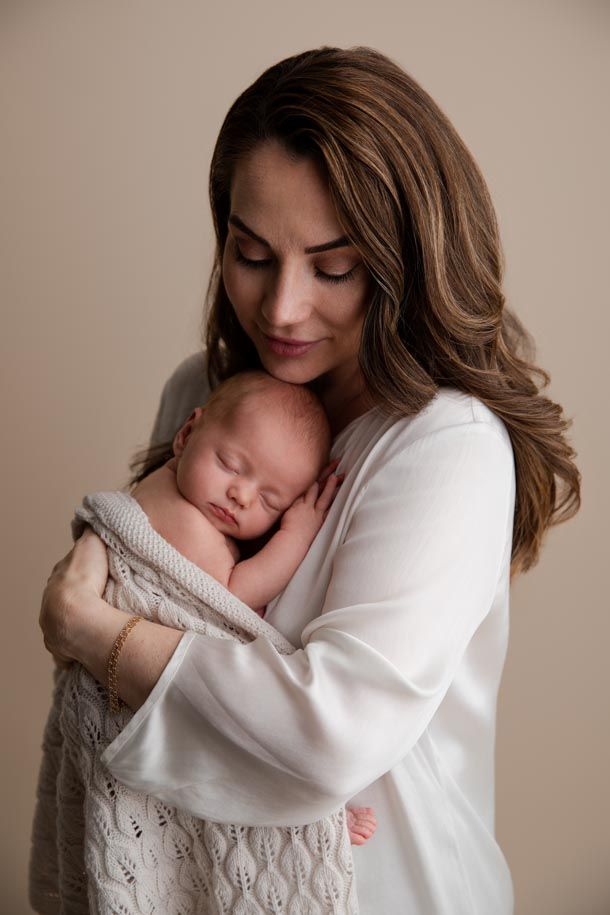 Nyf&oslash;dtfotografering - Mamma i hvit bluse holder nyf&oslash;dt jente i strikket teppe inntil seg. 